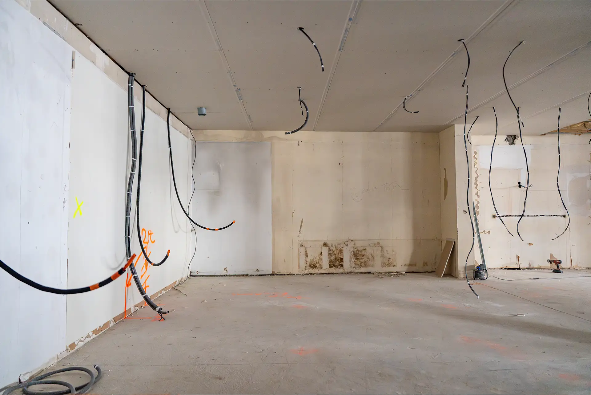 Blick auf eine Baustelle im Inneren eines Hauses, bei der während der Renovierung elektrische Kabel an Decke und Wänden freiliegen.